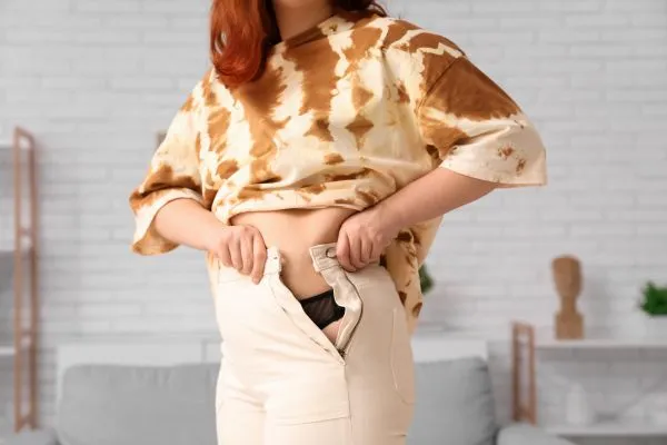 Image of woman trying to do her trousers up after pregnancy weight gain Christchurch